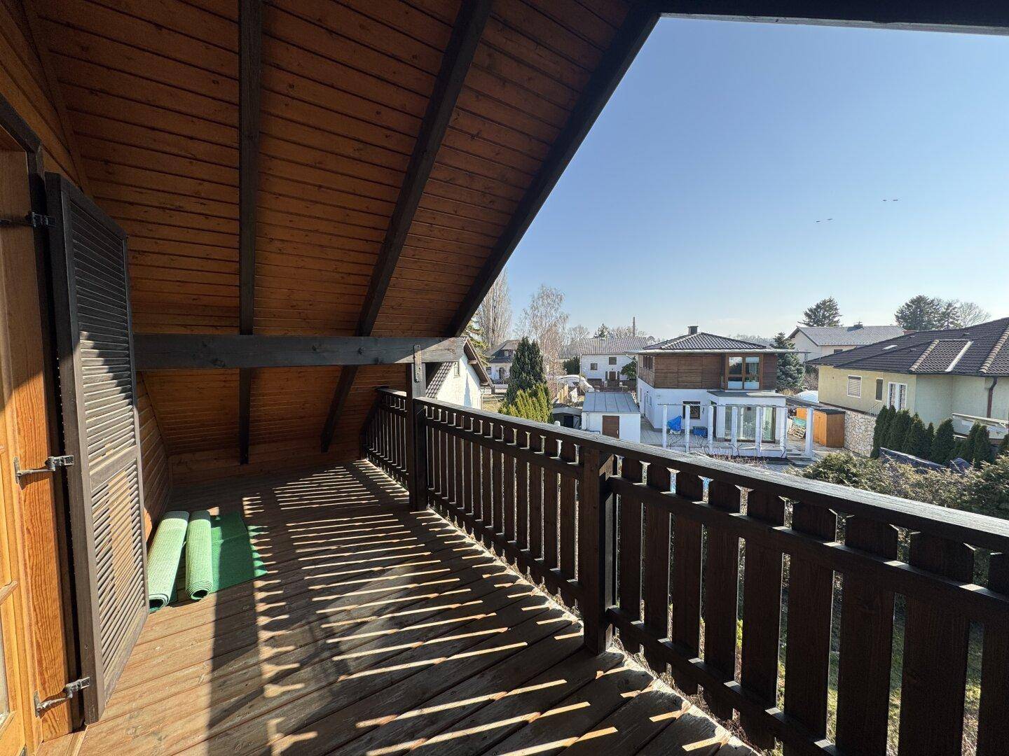 Geräumiger Holzbalkon mit Blick auf die Nachbarschaft und viel Sonnenlicht am Nachmittag.