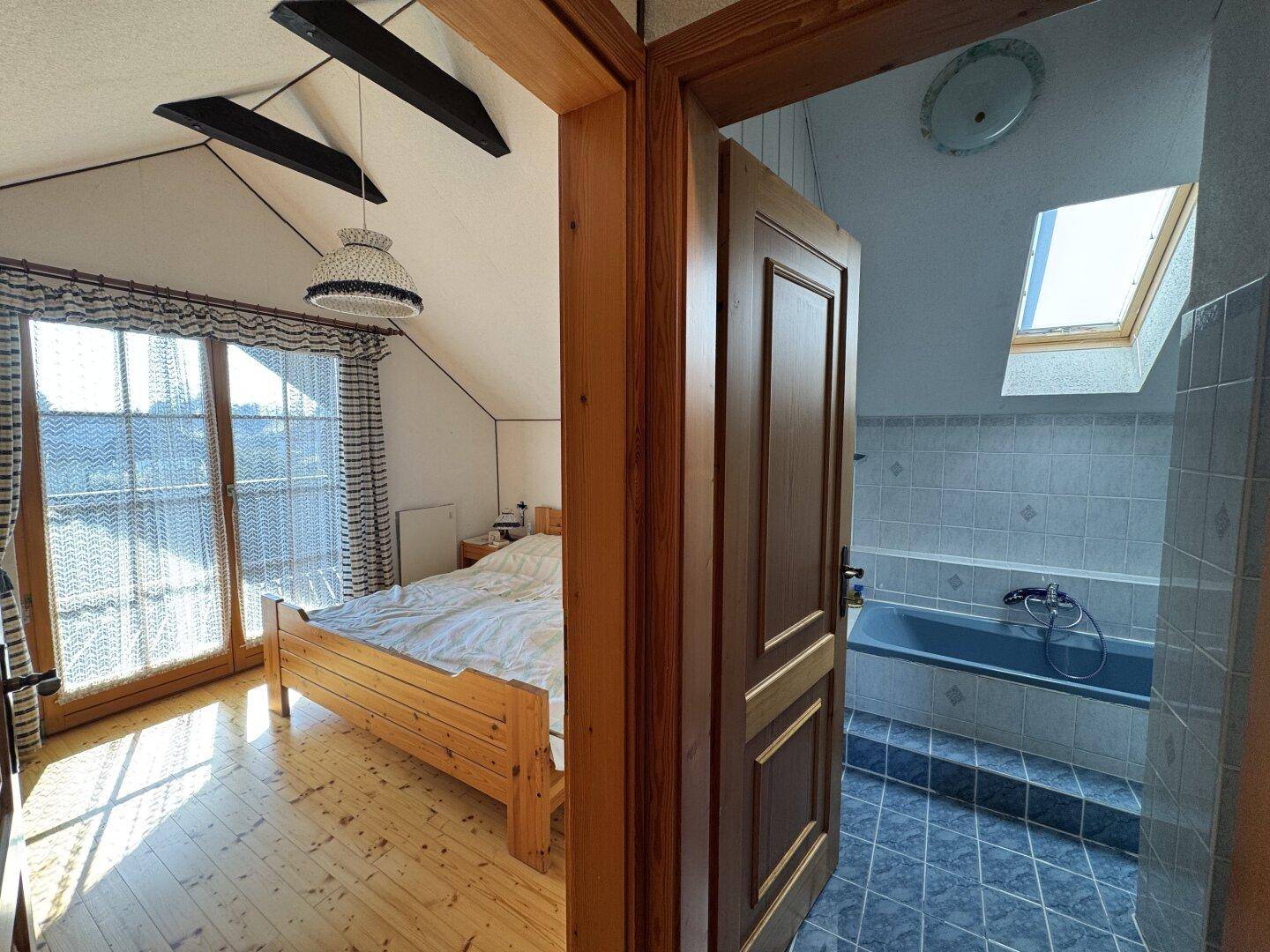 Blick durch die Tür von einem Schlafzimmer in ein gefliestes Badezimmer mit Dachfenster.