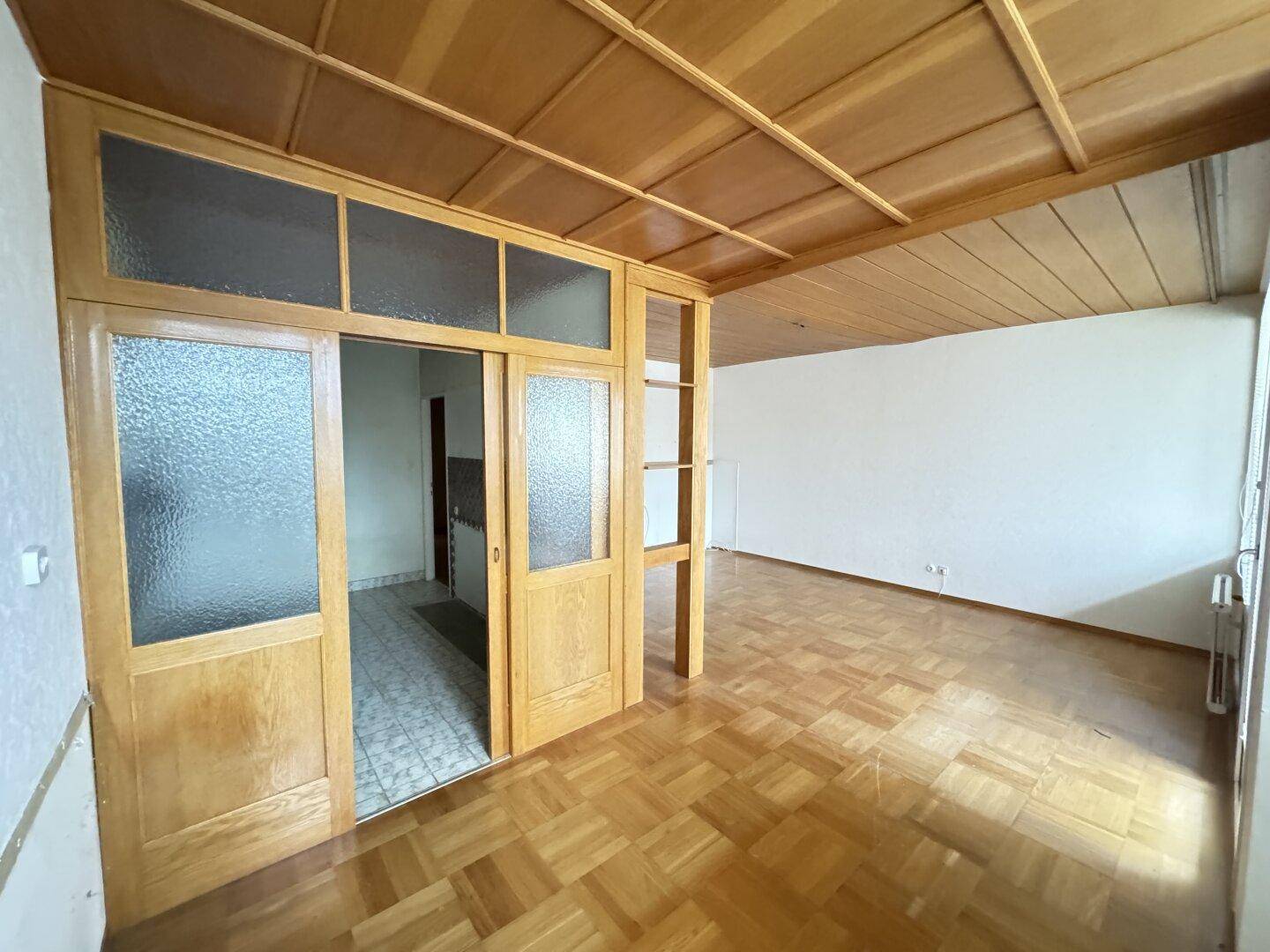 Heller Raum mit Parkettboden und Holztüren, die zu einem weiteren Bereich führen.
