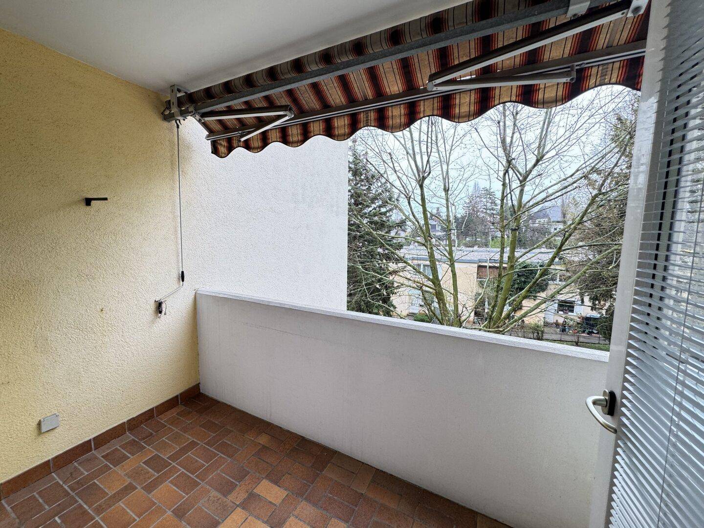Kleiner Balkon mit Markise und Blick ins Grüne, ideal für entspannte Stunden.