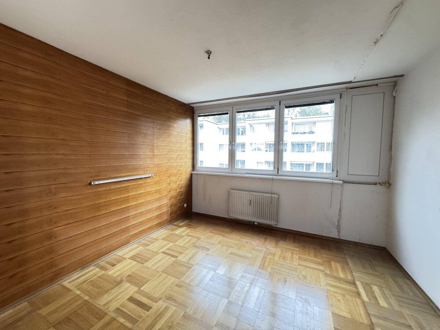 Leeres Schlafzimmer mit Holzwand, Parkettboden und großem Fenster.