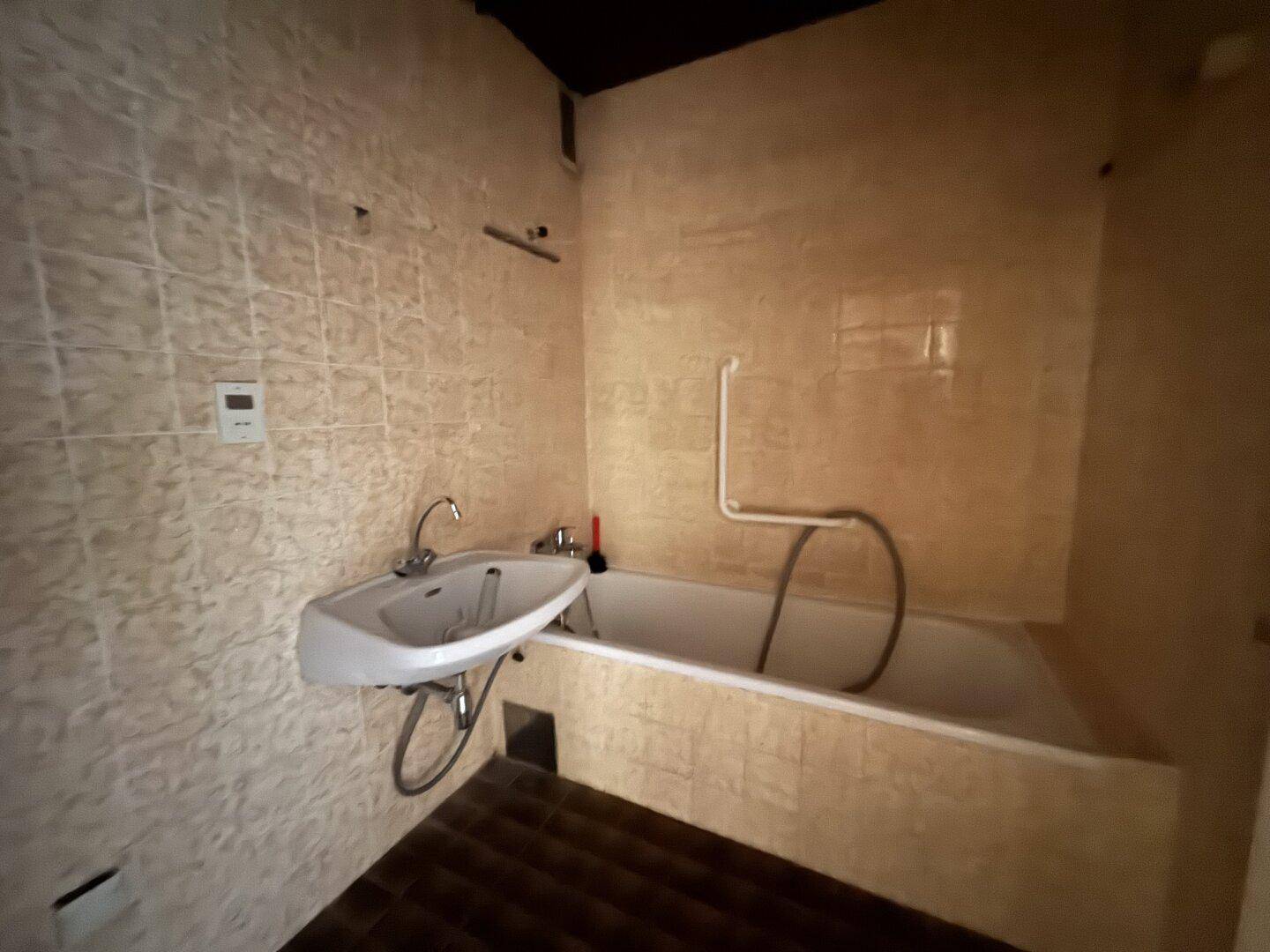 Badezimmer mit Badewanne, Fliesenwänden und einfacher Ausstattung.