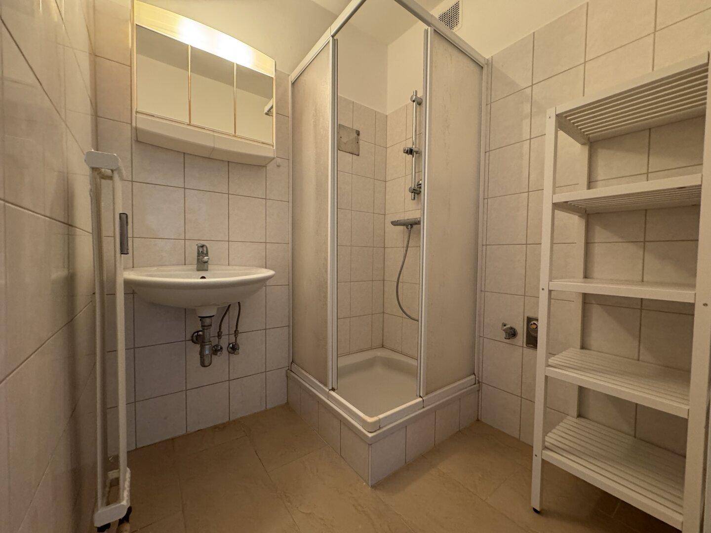 Badezimmer mit hellen Fliesen, einer Duschkabine, Waschbecken und einem Handtuchheizkörper.