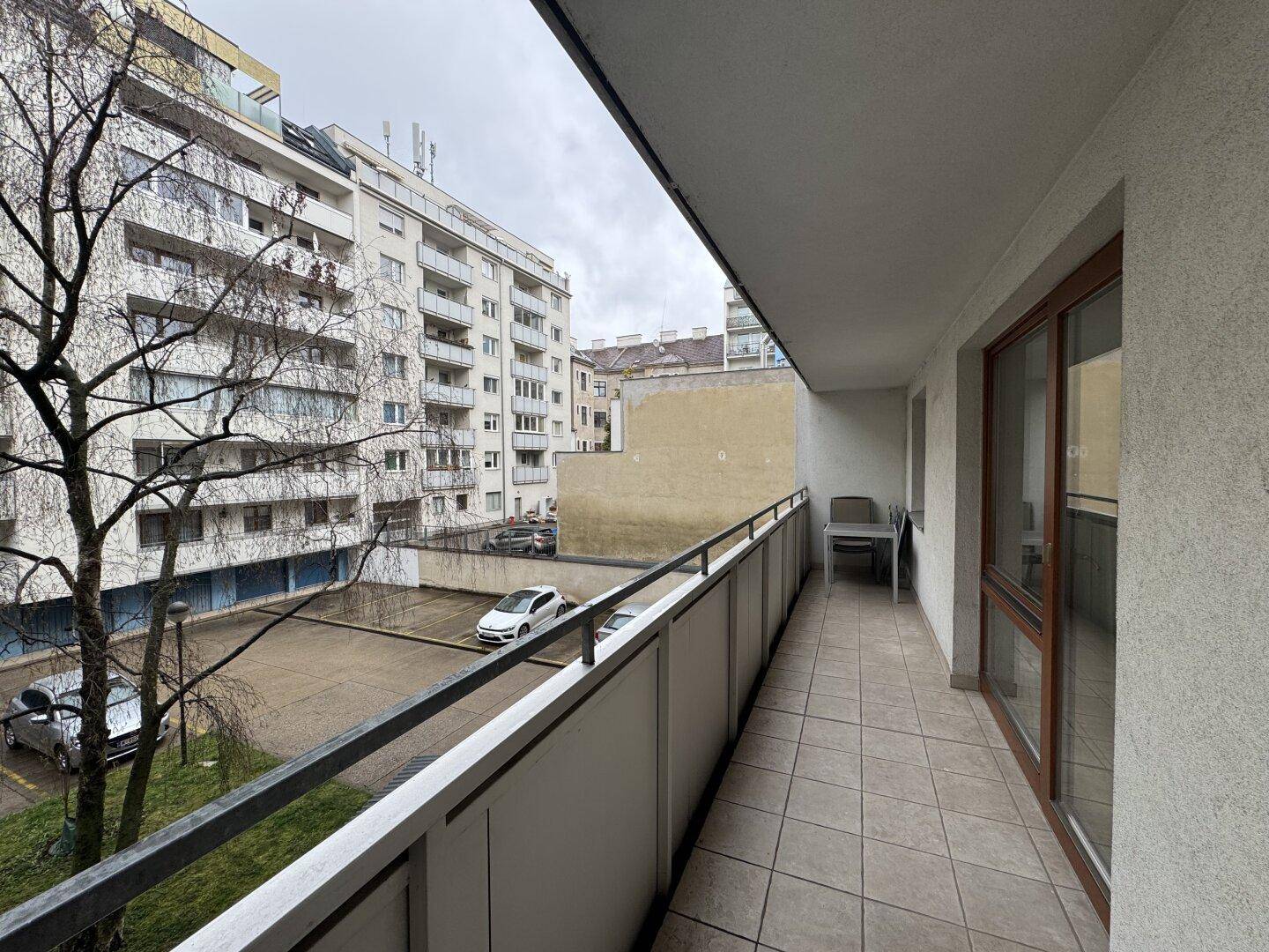 Langer, schmaler Balkon mit Fliesenboden und Metallgeländer, bietet Blick auf den Innenhof.