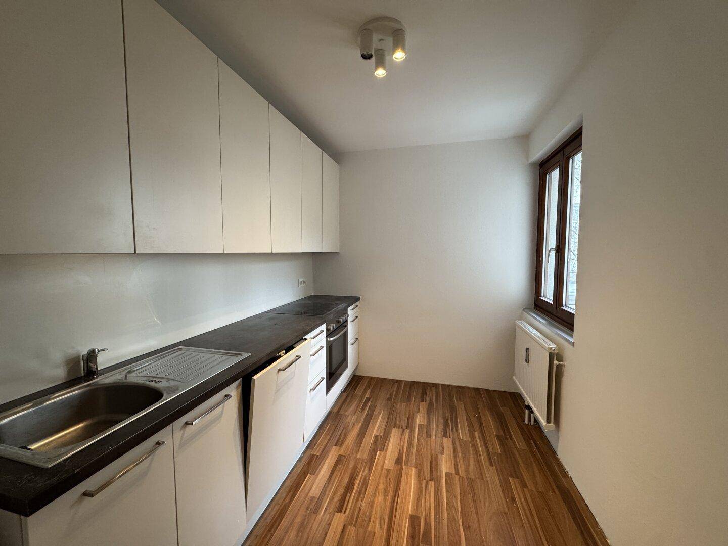 Funktionale Küche mit weißen Schränken, dunkler Arbeitsplatte, Spüle und Holzboden.