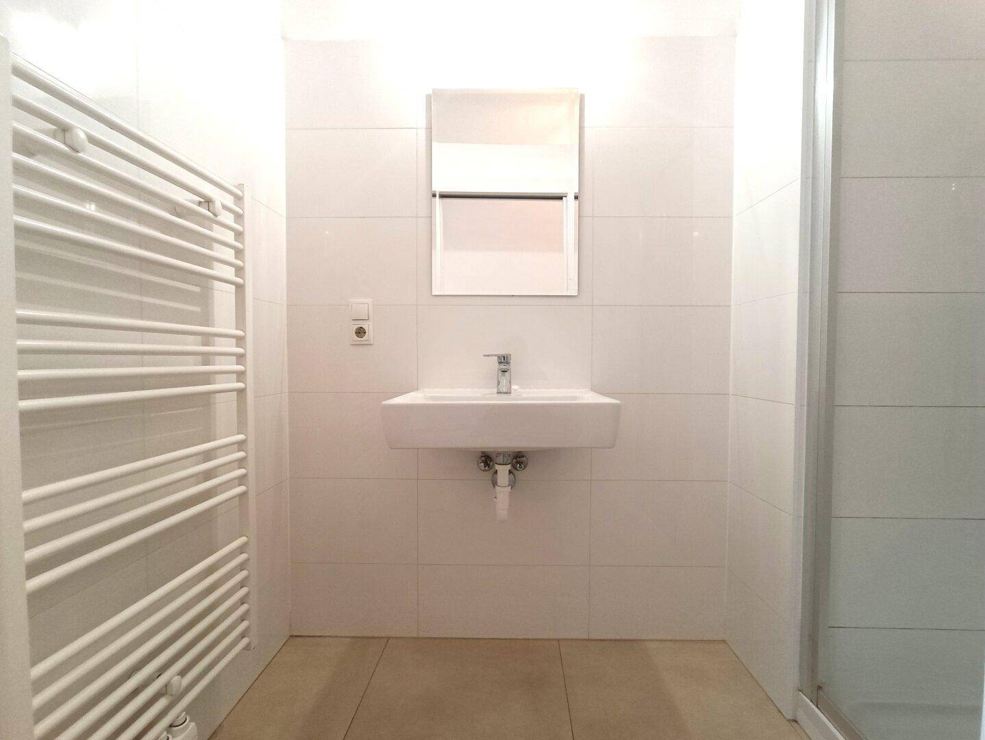 Modernes Badezimmer mit Waschbecken, Spiegel und beheiztem Handtuchhalter an der Wand.