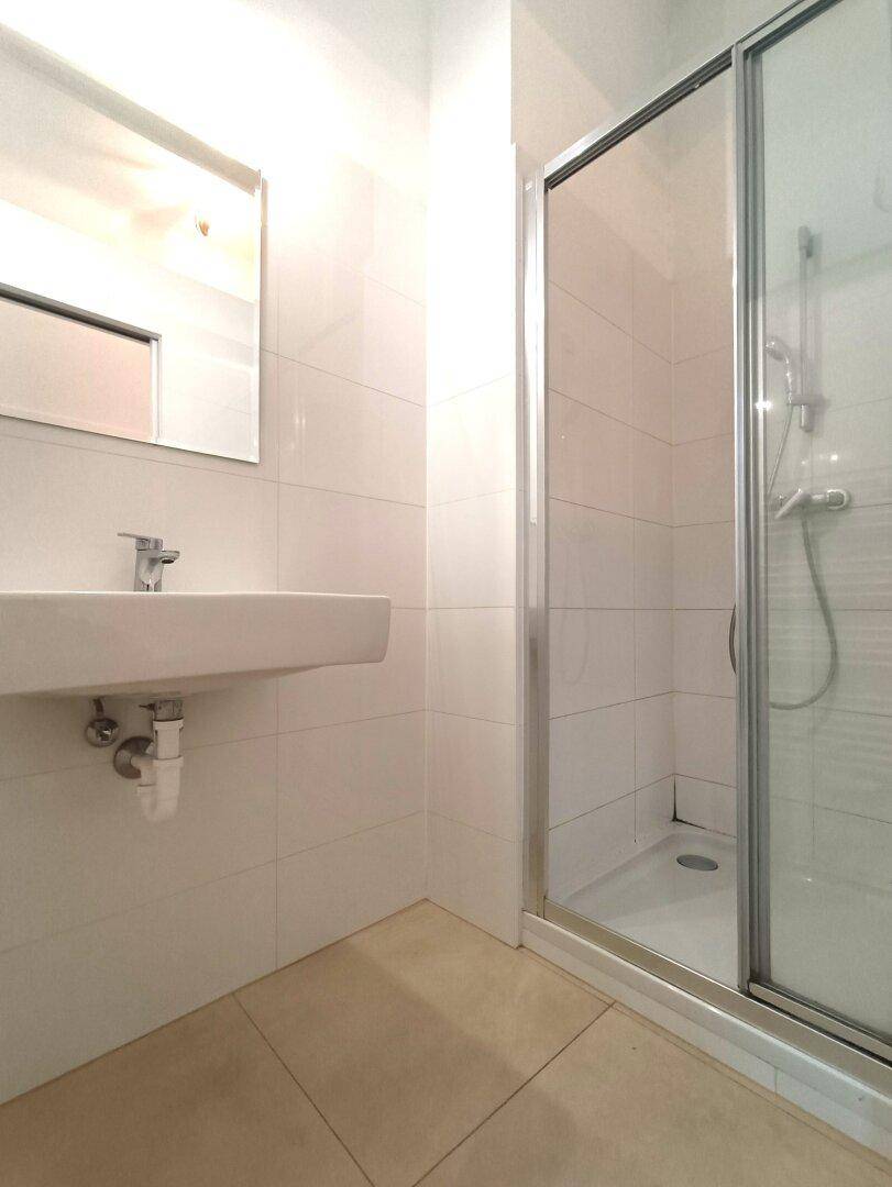 Helles Badezimmer mit Duschkabine, modernem Waschbecken und weißen Fliesen an den Wänden.