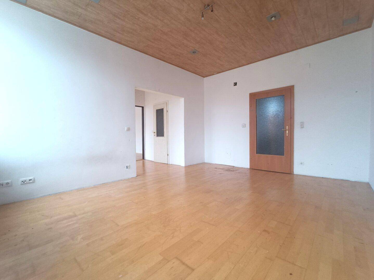 Leeres Zimmer mit Holzdecke und Parkettboden, bereit zur Renovierung.