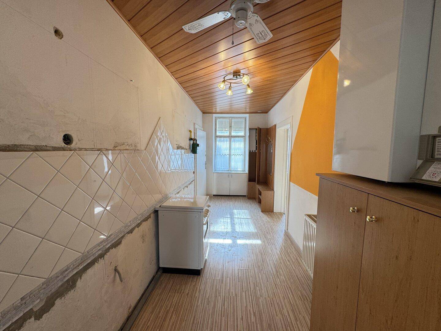 Renovierungsbedürftige Küche mit Holzdecke und Fliesenwand.