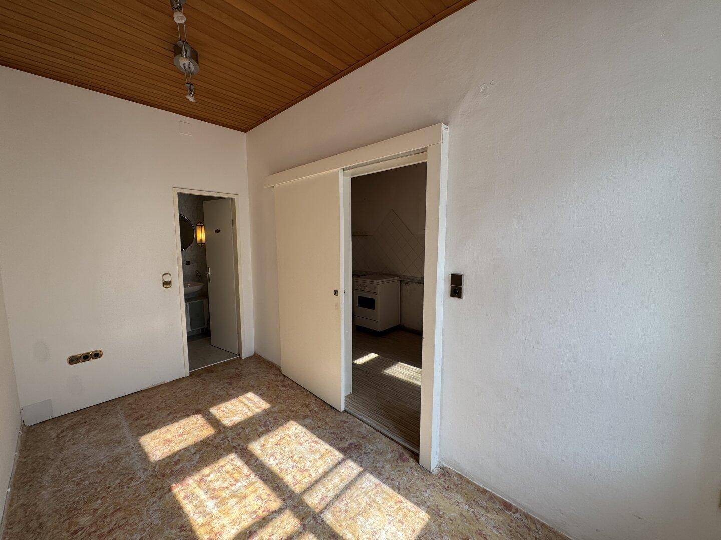 Kleiner Raum mit Holzdecke und Schiebetür, renovierungsbedürftig.