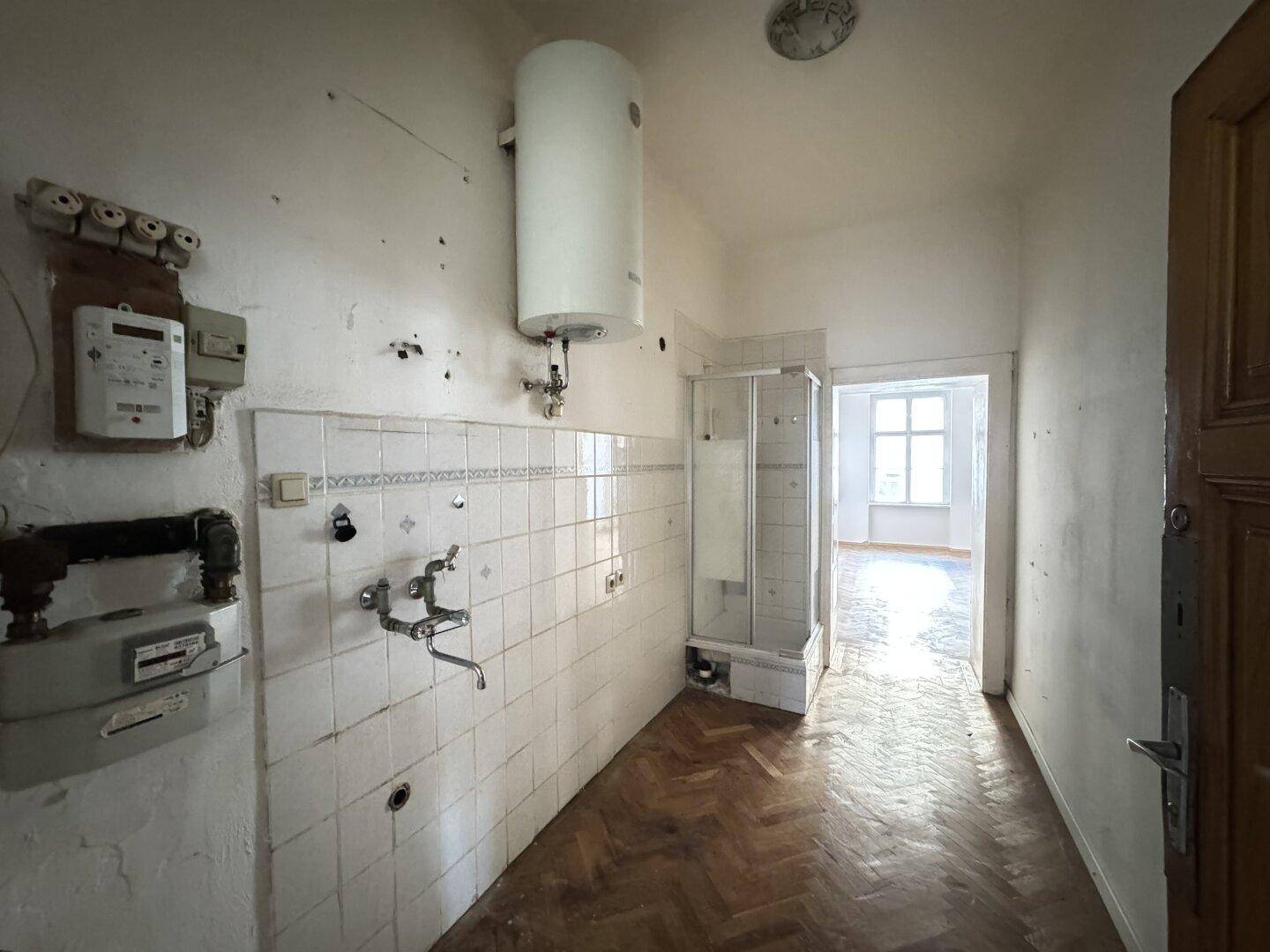 Sanierungsbedürftige Küche mit Boiler, Duschkabine und alten Fliesen.