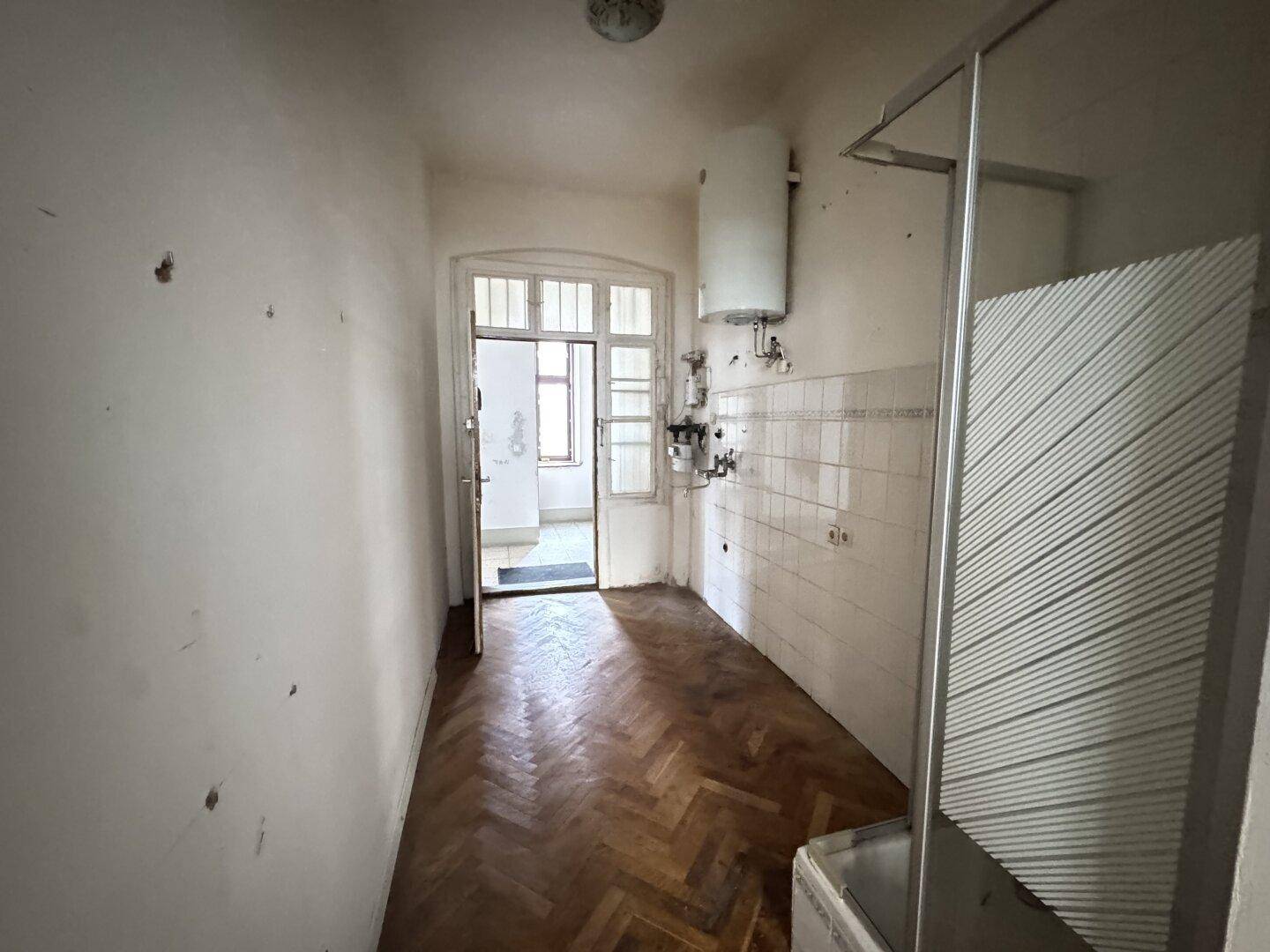 Sanierungsbedürftiger Küchenbereich mit Boiler, Duschkabine und Fenster.