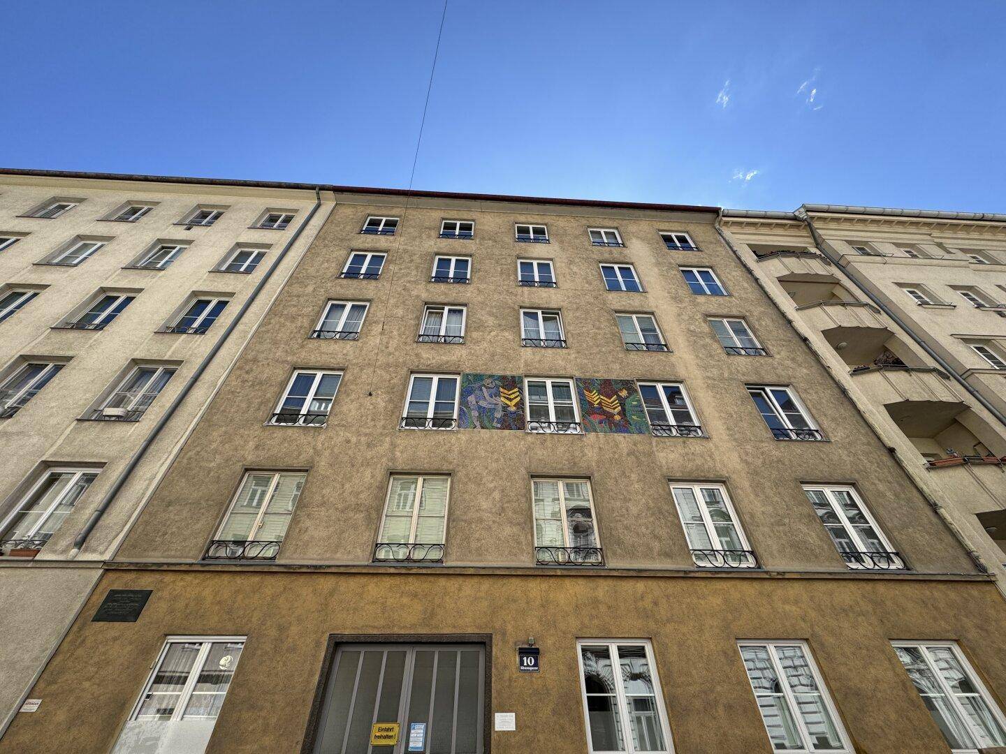 Fassade eines Mehrfamilienhauses mit mehreren Fenstern und einem farbigen Wandbild.