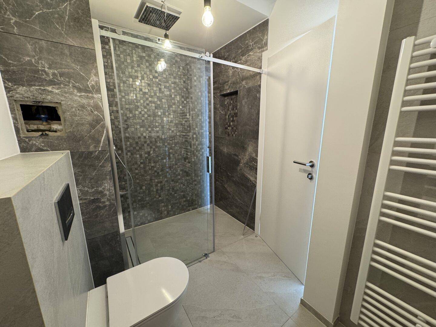 Modernes Badezimmer mit begehbarer Dusche, Wand-WC und eleganten dunklen Fliesen.