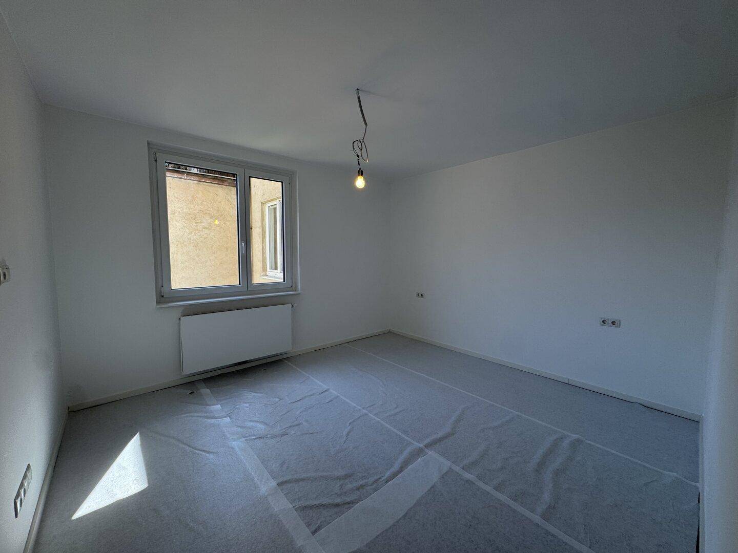 Leerer Raum mit Fenster und abgedecktem Boden, bereit für die weitere Gestaltung.