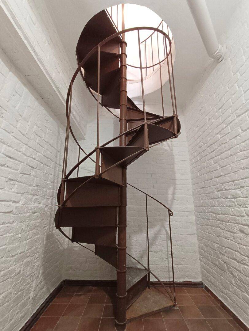 Detailansicht der Wendeltreppe in einem Raum mit weiß gestrichenen Ziegelwänden und Terrakottafliesen.
