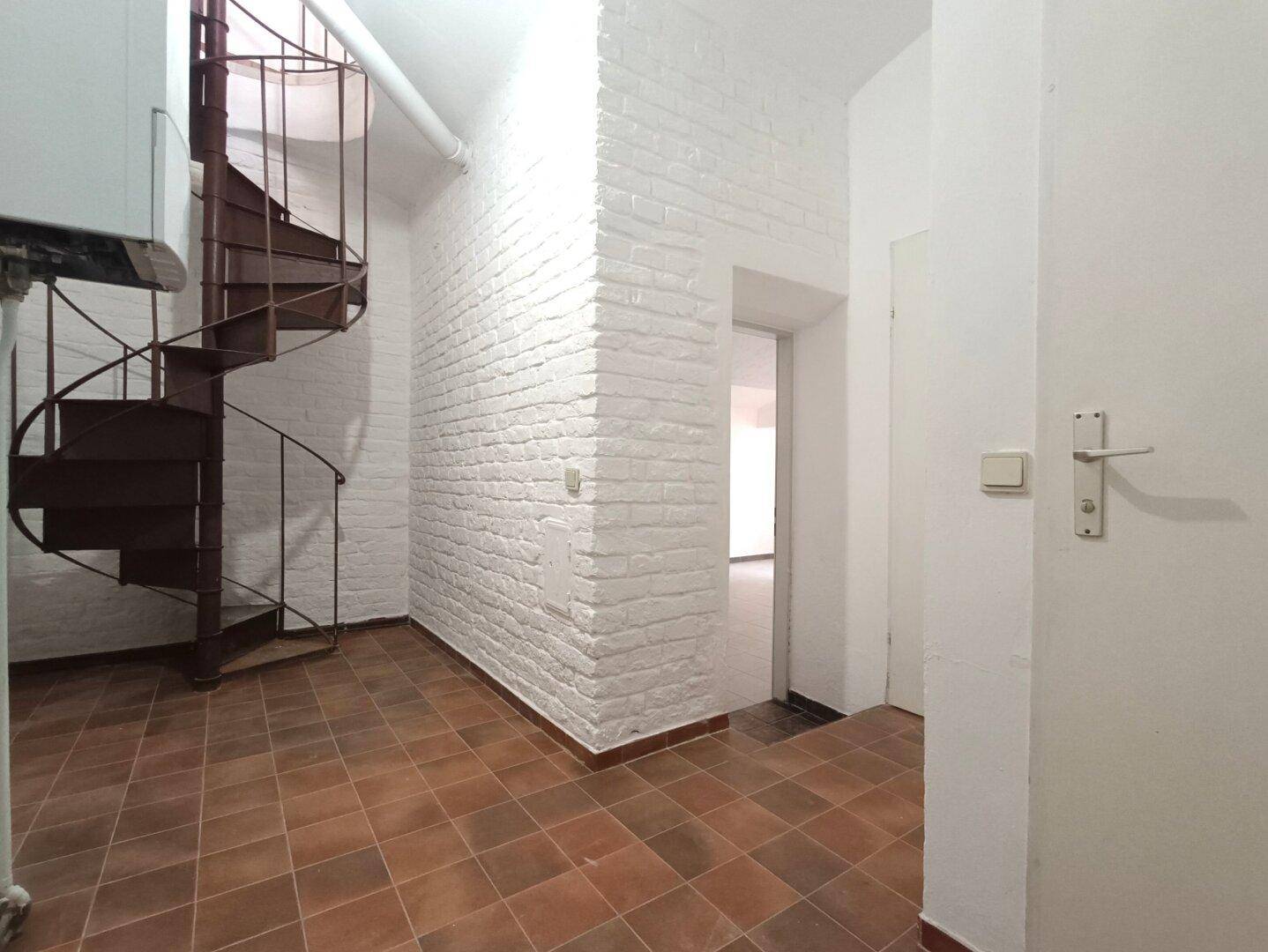 Flur mit Terrakottafliesen, einer Wendeltreppe und einer weiß gestrichenen Ziegelwand.