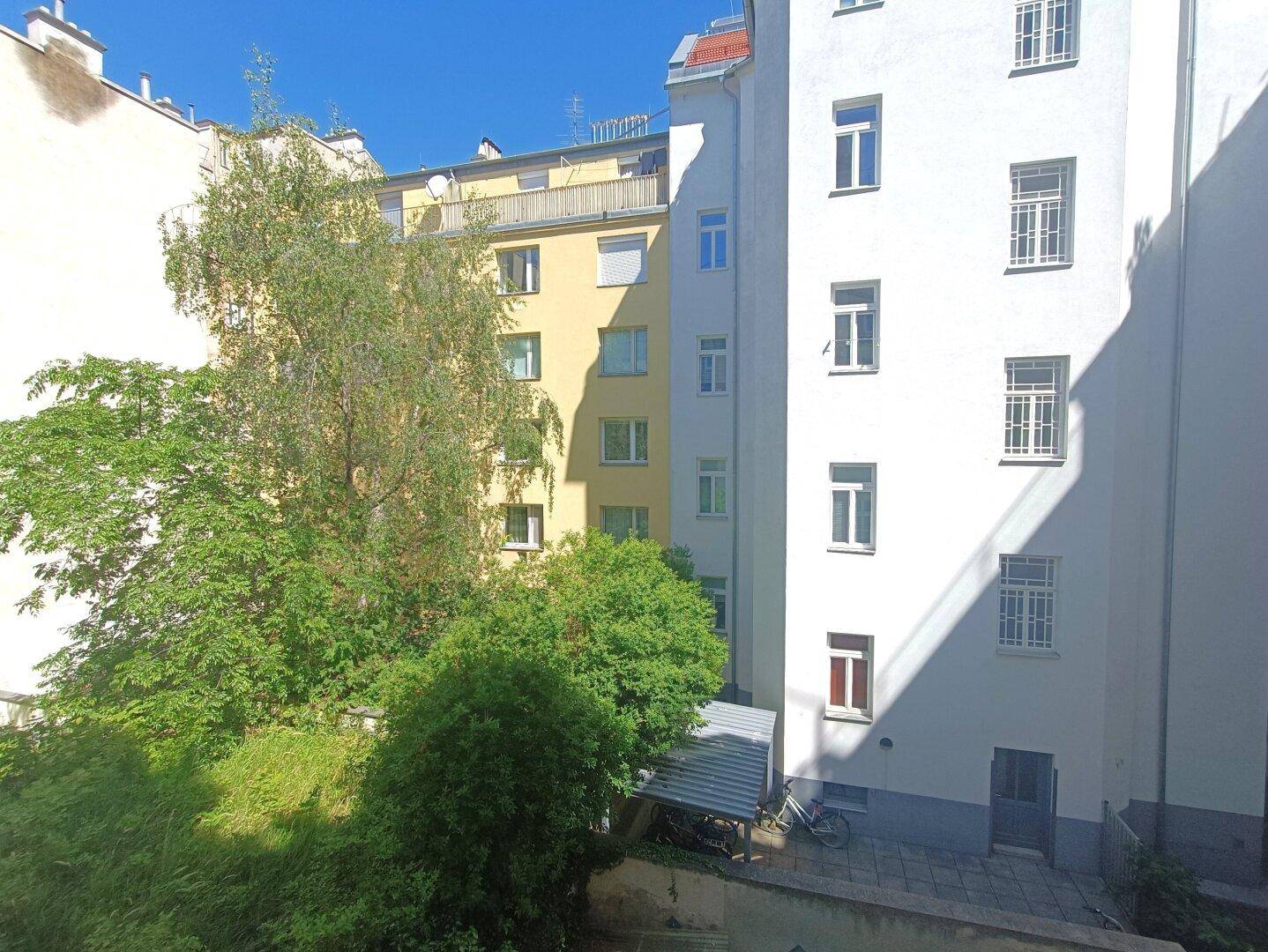 Blick von einem Balkon in einen grünen Innenhof mit Bäumen und angrenzenden Gebäuden.