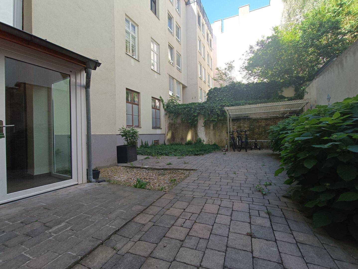 Gepflasterter Innenhof mit Fahrradabstellplatz und begrünten Wänden, umgeben von Gebäuden.