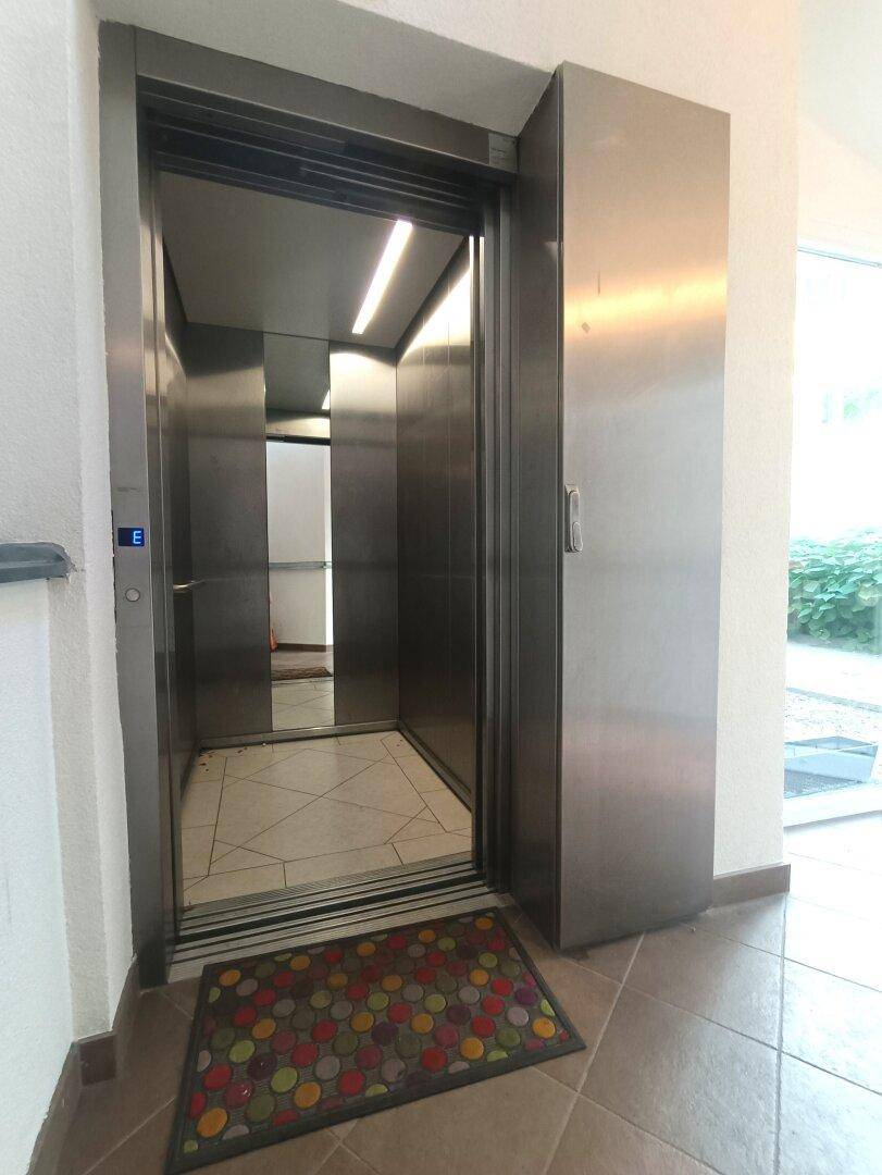 Moderner Aufzug mit Edelstahloberflächen und gefliestem Boden in einem Gebäude.