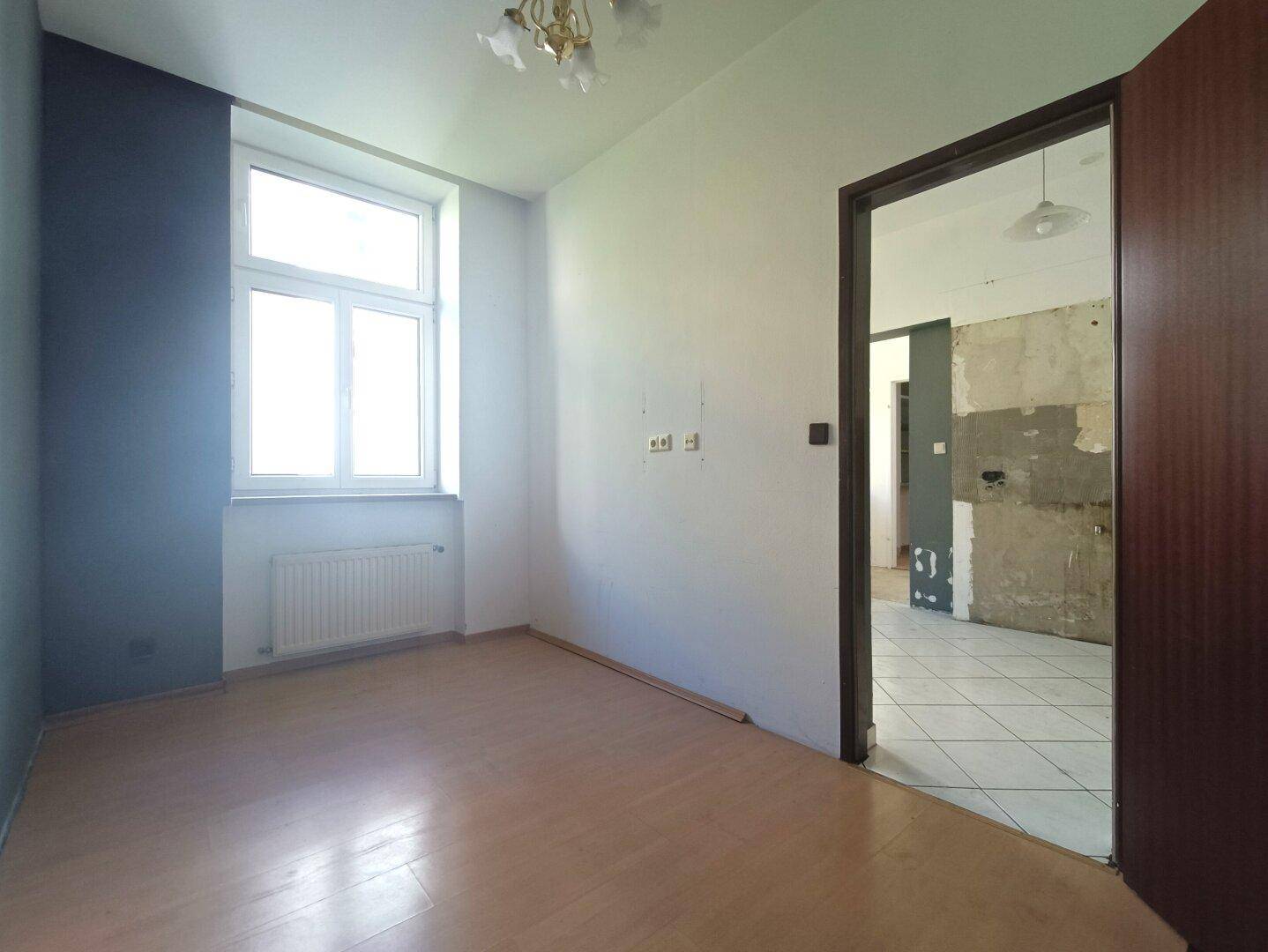 Heller, leerer Raum mit Laminatboden und einem Fenster, bereit für die individuelle Gestaltung.