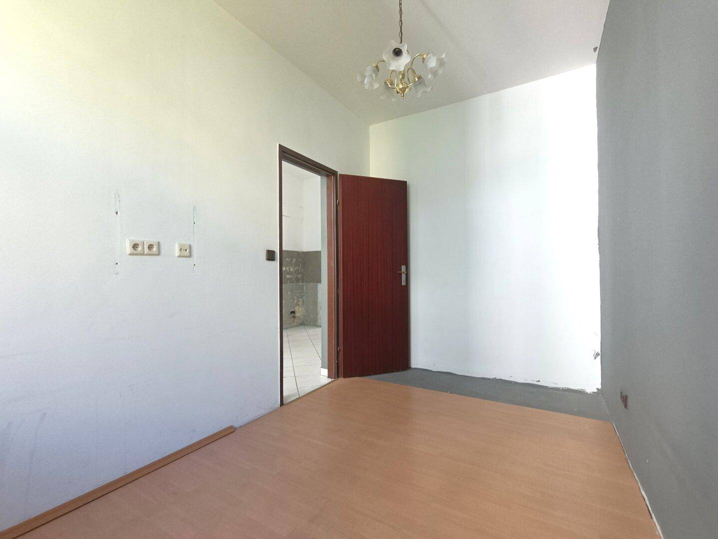 Leerer Raum mit Laminatboden und einer Holztür, die zu einem weiteren Zimmer führt.