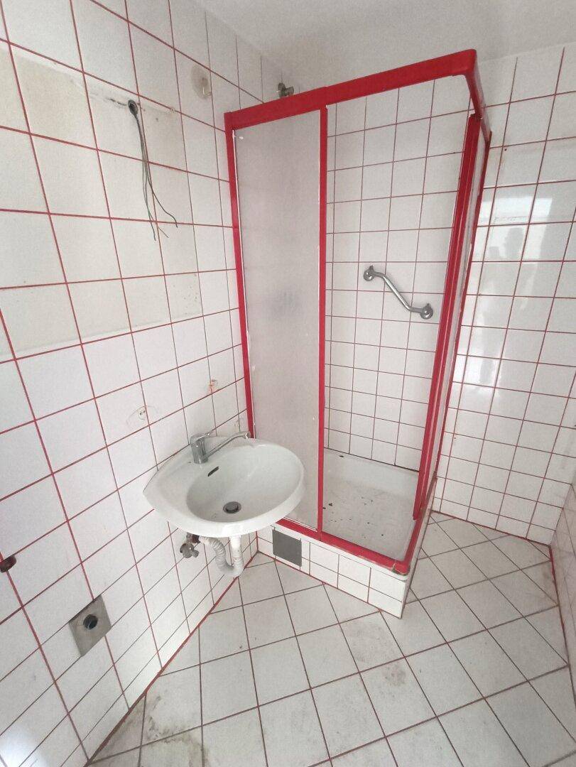 Kleines Badezimmer mit roten Fliesen, Waschbecken, Duschkabine und Haltegriffen.