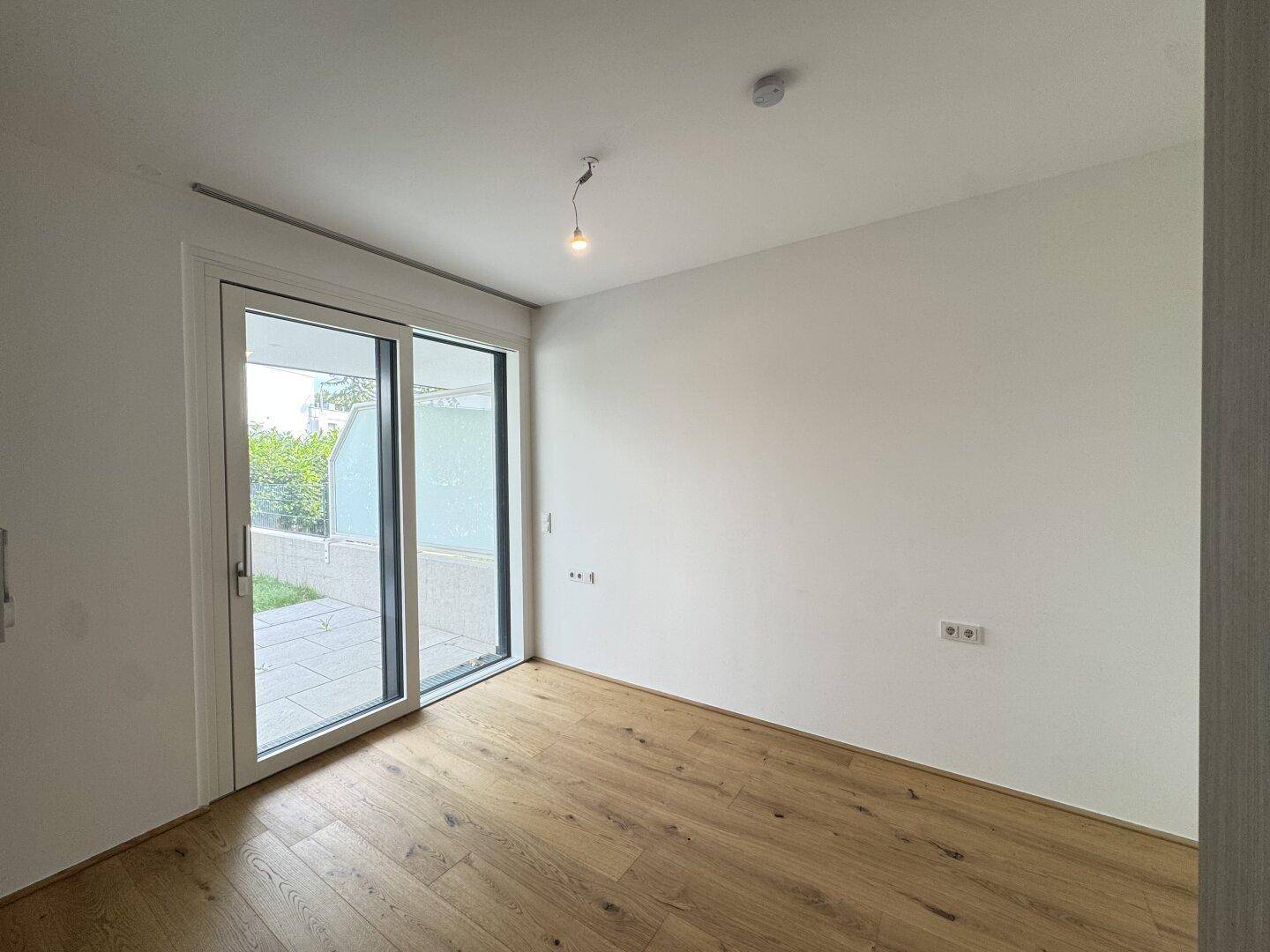 Leerer Raum mit Holzboden und großer Schiebetür, die zu einer Terrasse führt.