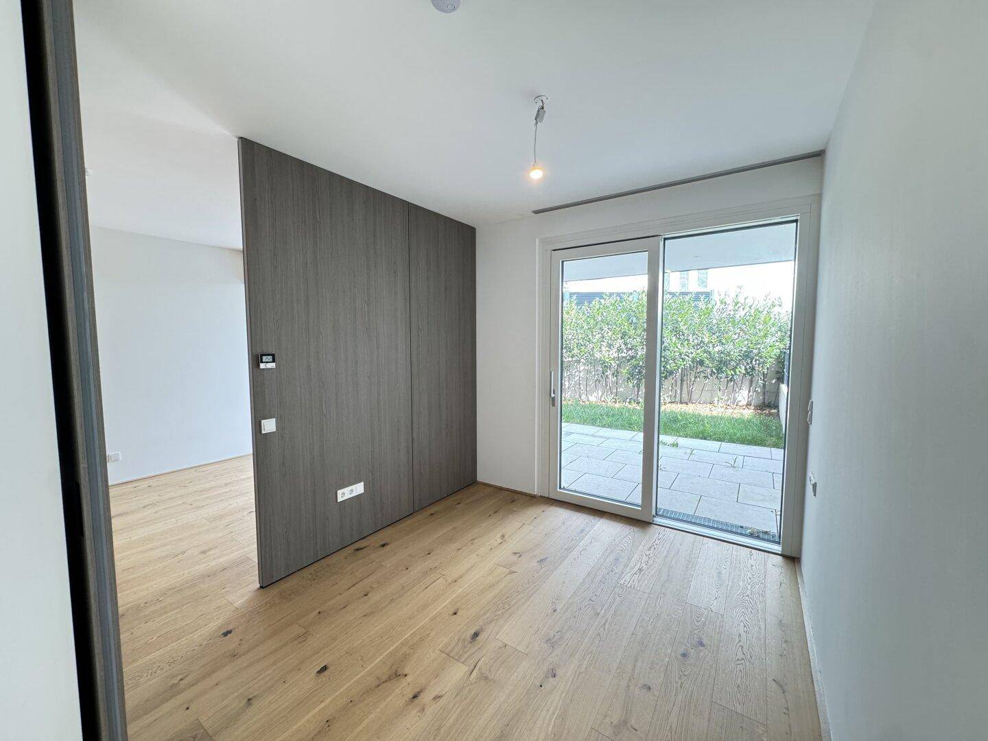 Heller Raum mit Holzboden, Einbauschrank und Zugang zu einer kleinen Grünfläche.