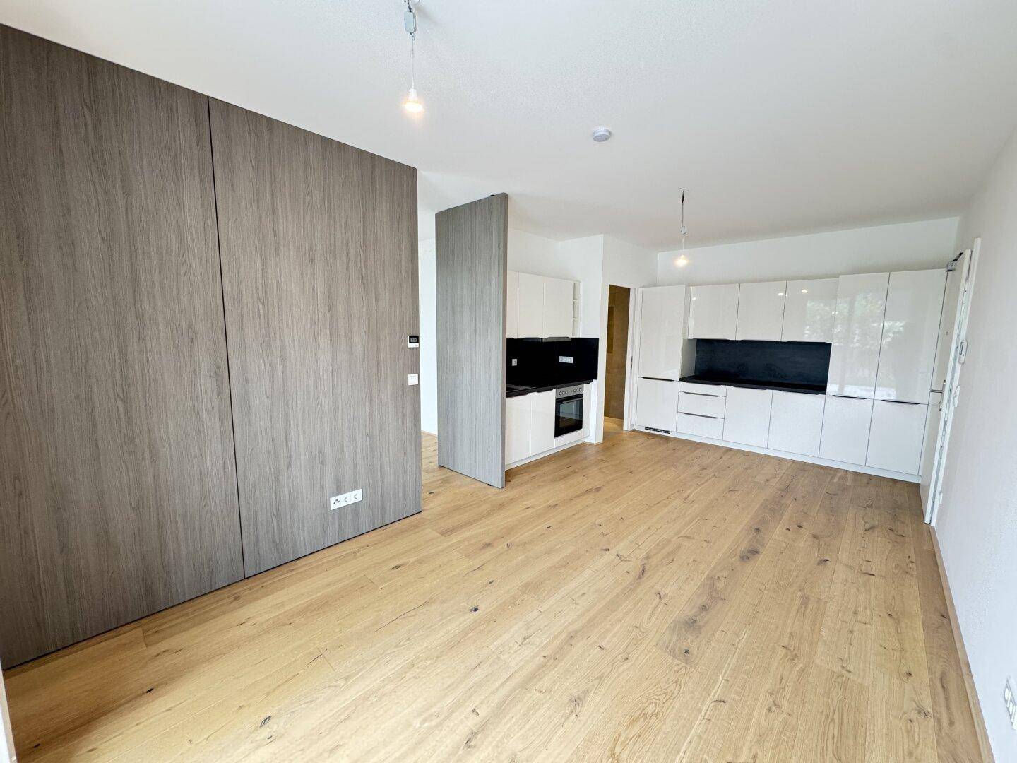Heller offener Raum mit Holzboden und vorbereiteter Küche in modernem Design.