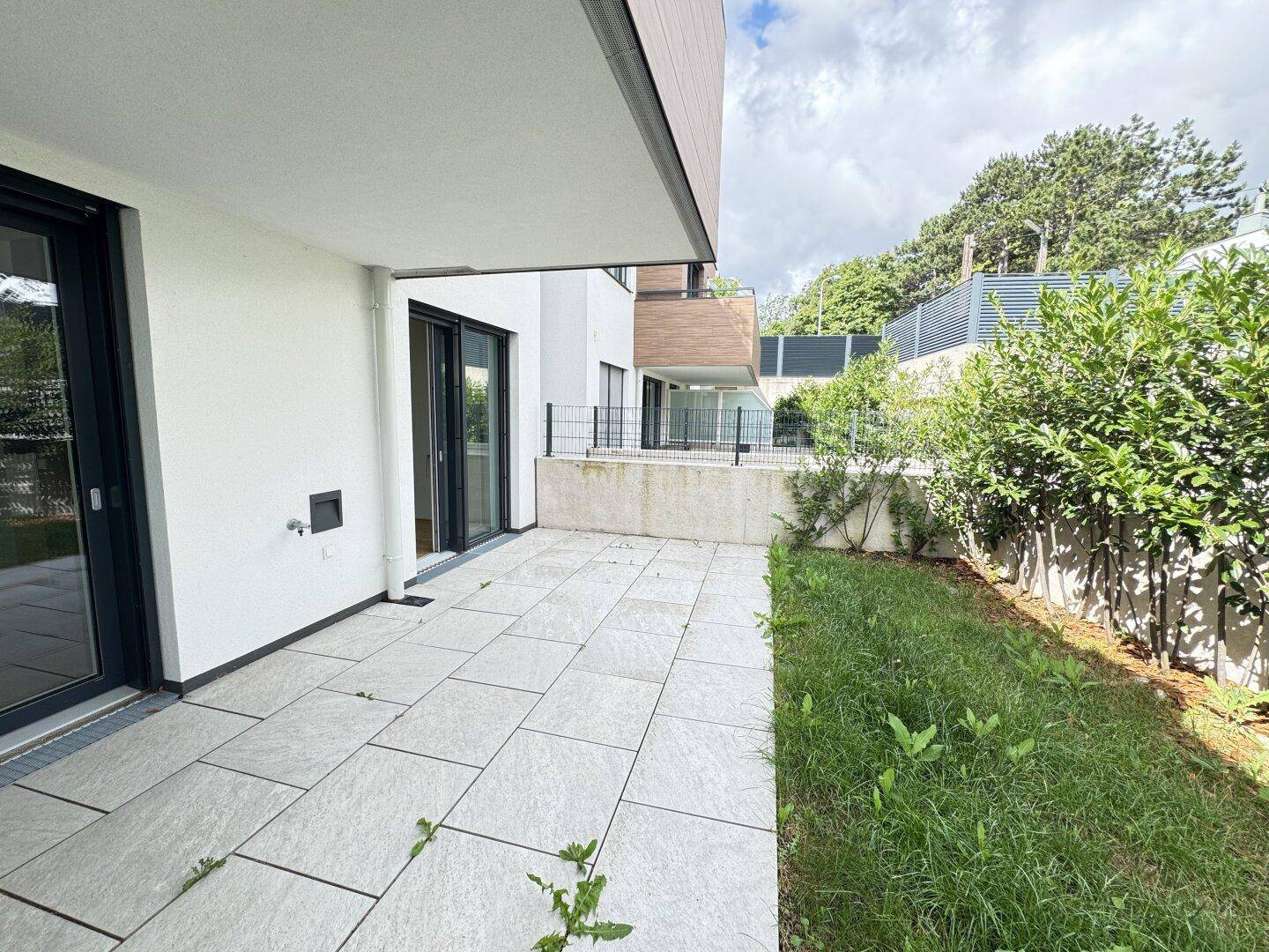 Geräumige Terrasse mit Fliesenboden und angrenzendem Gartenbereich unter bewölktem Himmel.