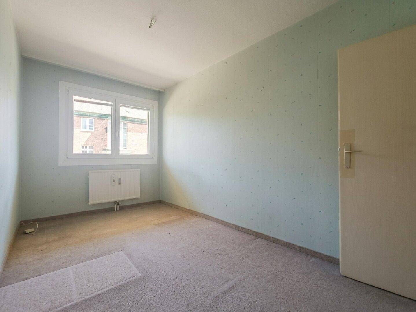 Helles Schlafzimmer mit hellblau gestrichenen Wänden und Teppichboden.