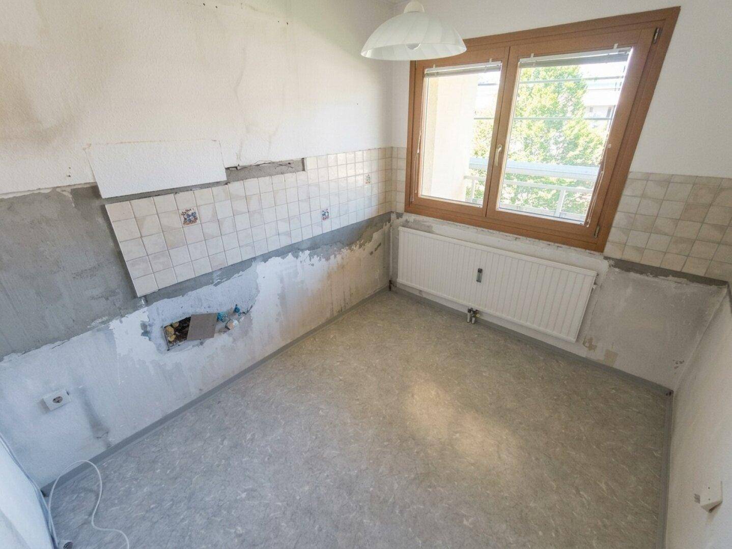 Leere Küche in Renovierung mit alten Fliesen und Fenster, bereit für eine neue Einrichtung.