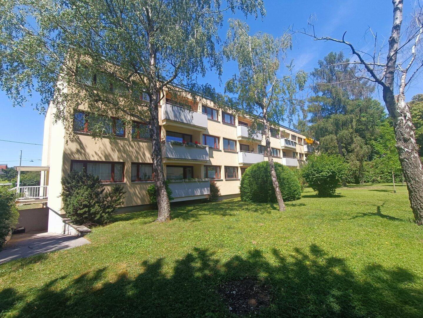Außenansicht eines Mehrfamilienhauses mit gepflegter Rasenfläche und Bäumen im Vorgarten.