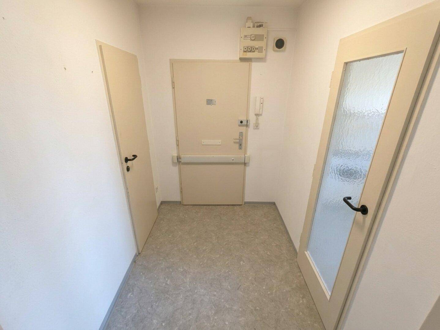Eingangsbereich mit mehreren Türen, Gegensprechanlage und strapazierfähigem Bodenbelag.