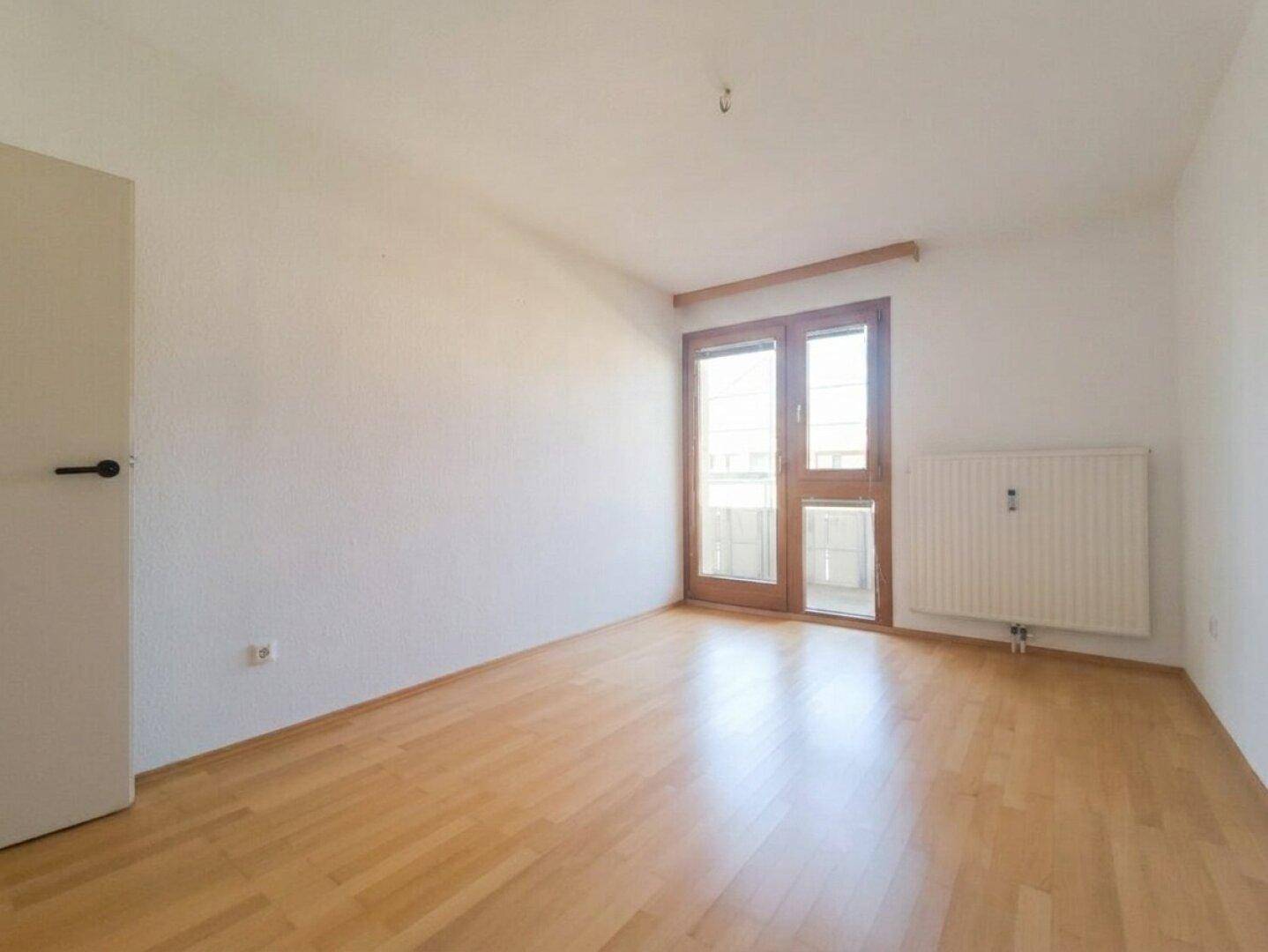 Helles Zimmer mit Parkettboden und Zugang zu einem kleinen Balkon oder französischen Balkon.