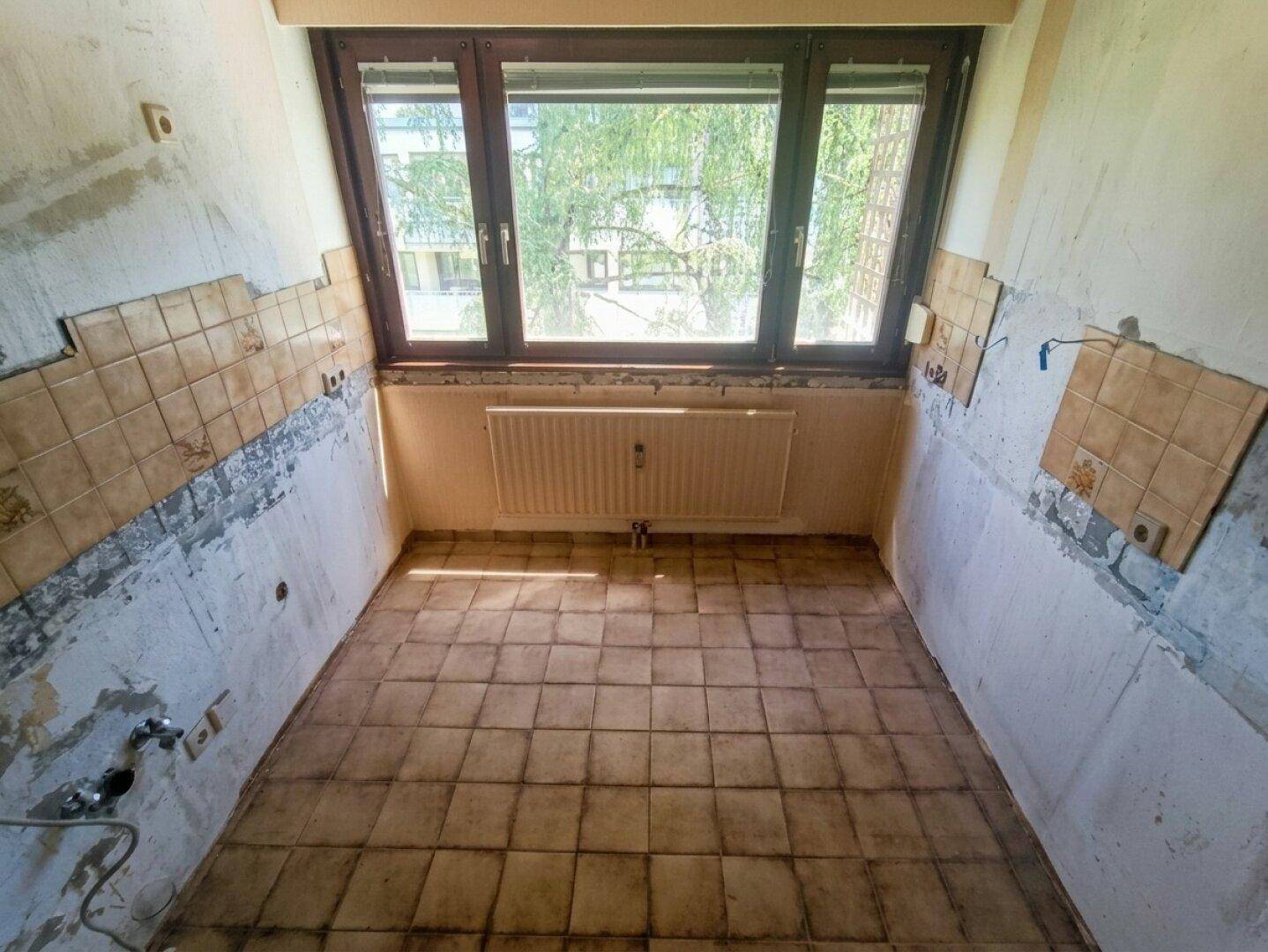 Küche in Renovierung mit Fliesenboden und Fenster, bereit für neue Einbauten.