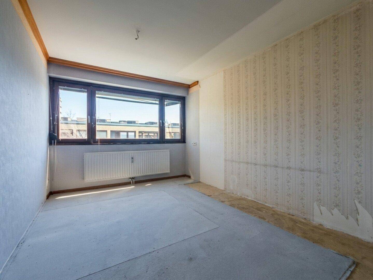 Leeres Zimmer mit Fenster und abziehbarer Tapete, bereit zur Renovierung.