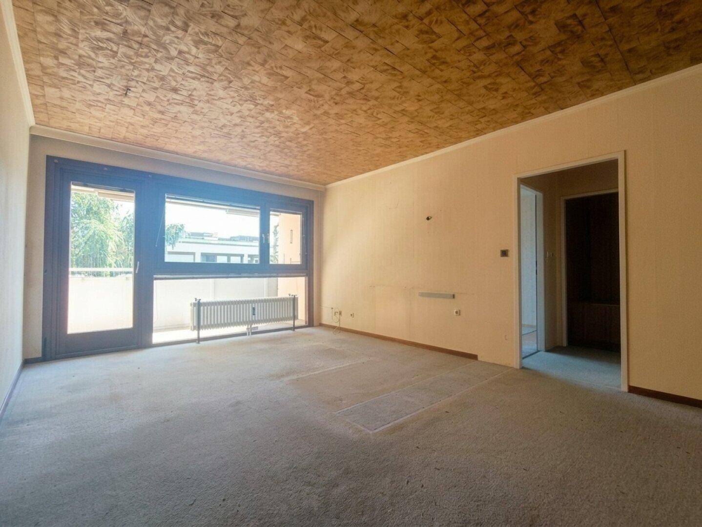 Geräumiges Wohnzimmer mit Zugang zum Balkon und einer strukturierten Decke.