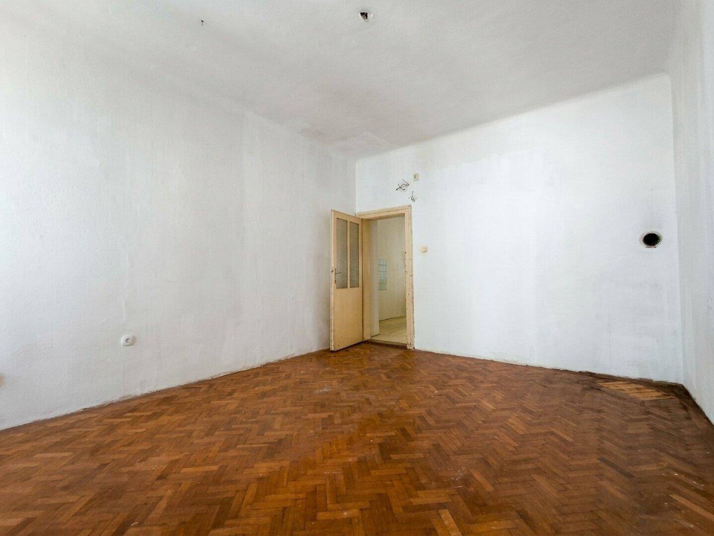 Helles, leeres Zimmer mit klassischem Fischgrätparkett und Zugang zu einem weiteren Raum.