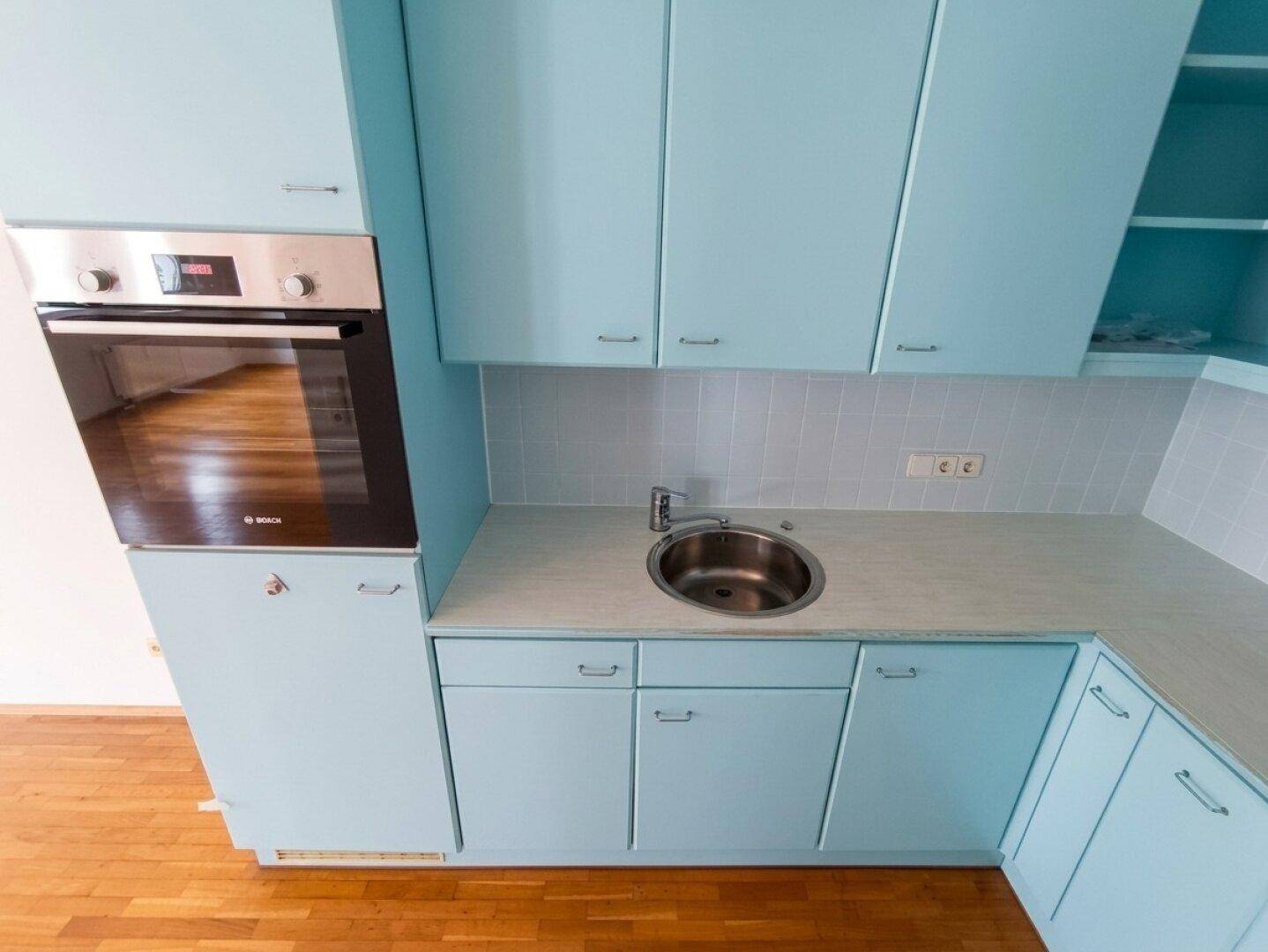 Detailansicht der Küche mit Edelstahlspüle, eingebautem Backofen und hellblauen Unterschränken.