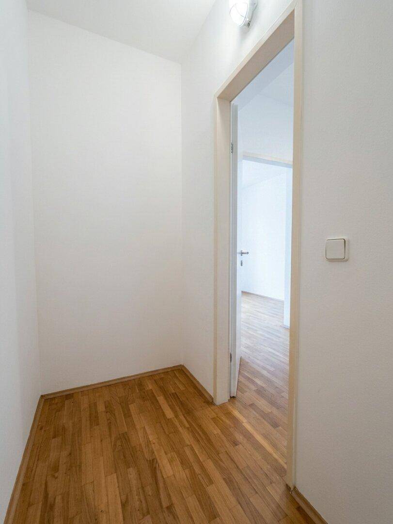 Schlichter Eingangsbereich mit Parkettboden und weiß gestrichenen Wänden, der einen offenen Durchgang bietet.