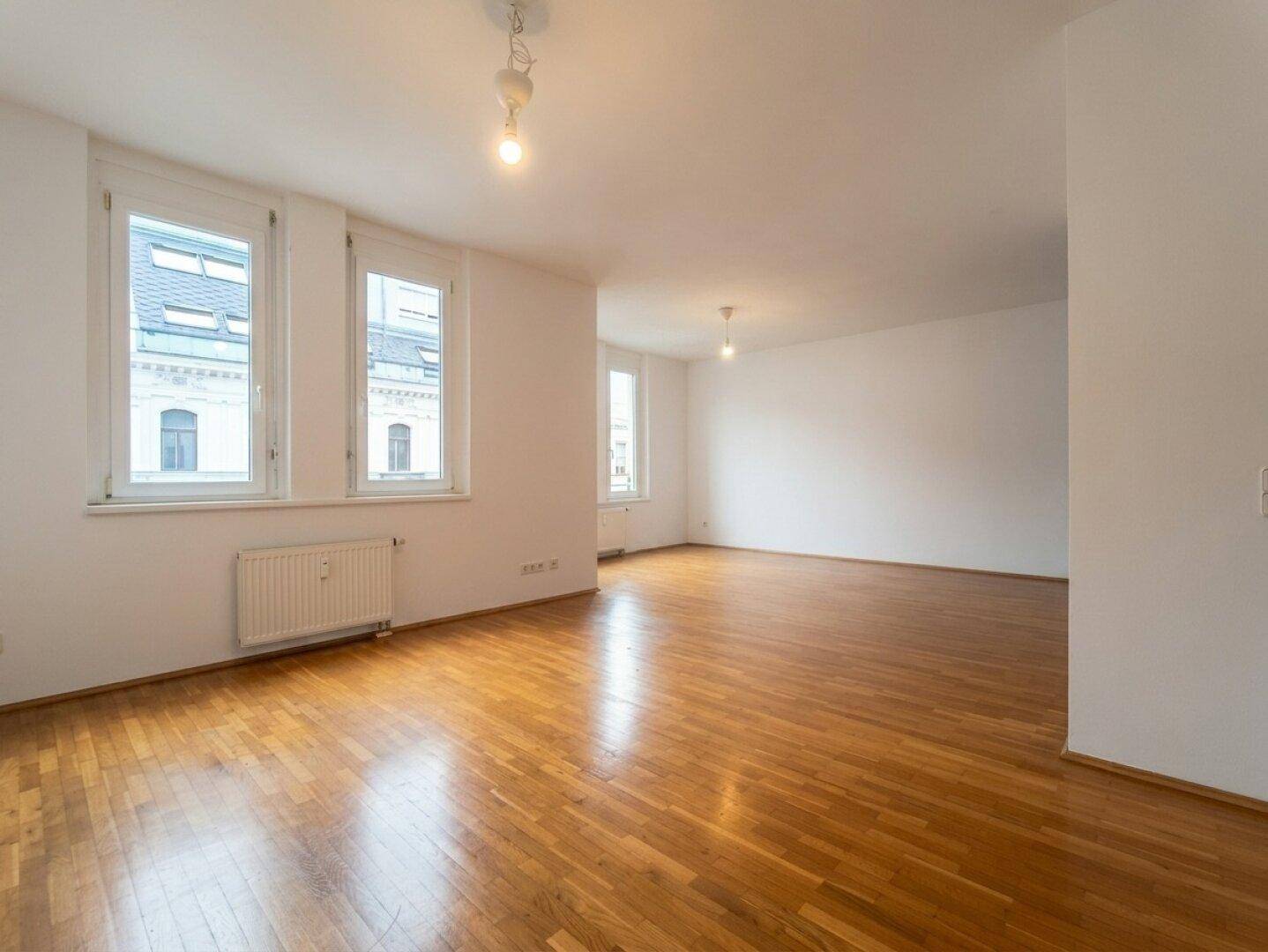 Heller Wohnraum mit klassischem Parkettboden und großen Fenstern, die den Blick nach draußen freigeben.