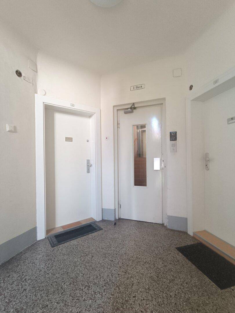 Heller Hausflur mit Zugang zu Wohnungen und einem Aufzug im zweiten Stock des Gebäudes.