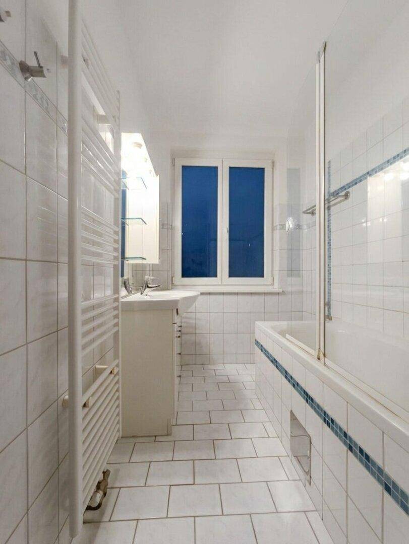 Gefliestes Badezimmer mit Badewanne, Waschbecken, Fenster und praktischem Handtuchheizkörper.