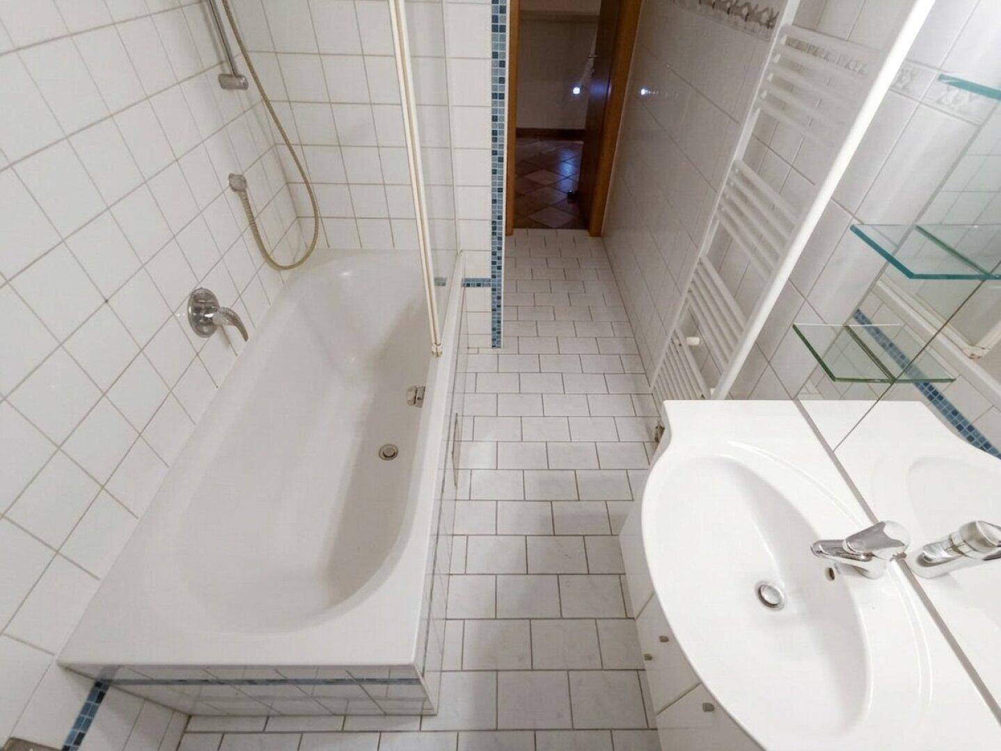 Badezimmer mit Badewanne und Duschvorrichtung, weiß gefliest mit blauen Akzenten und modernem Waschbecken.