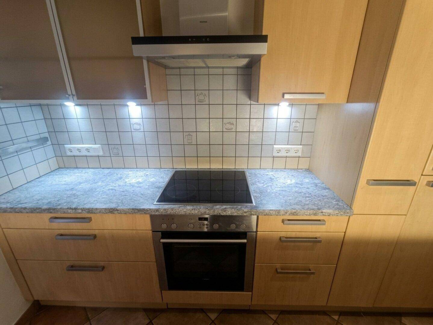 Integrierter Backofen und Cerankochfeld unter einer Dunstabzugshaube in der funktionalen Küche.