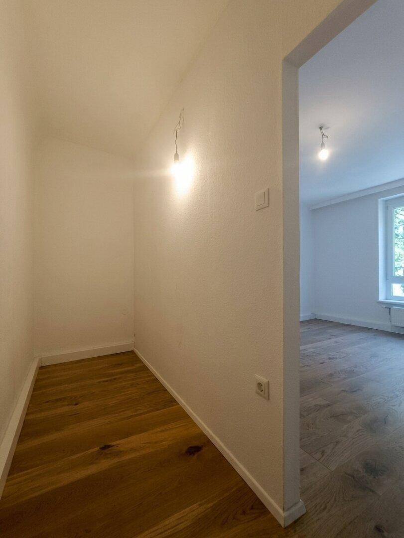 Heller Flurbereich mit Holzboden, der zu einem weiteren Zimmer führt und viel Licht bietet.