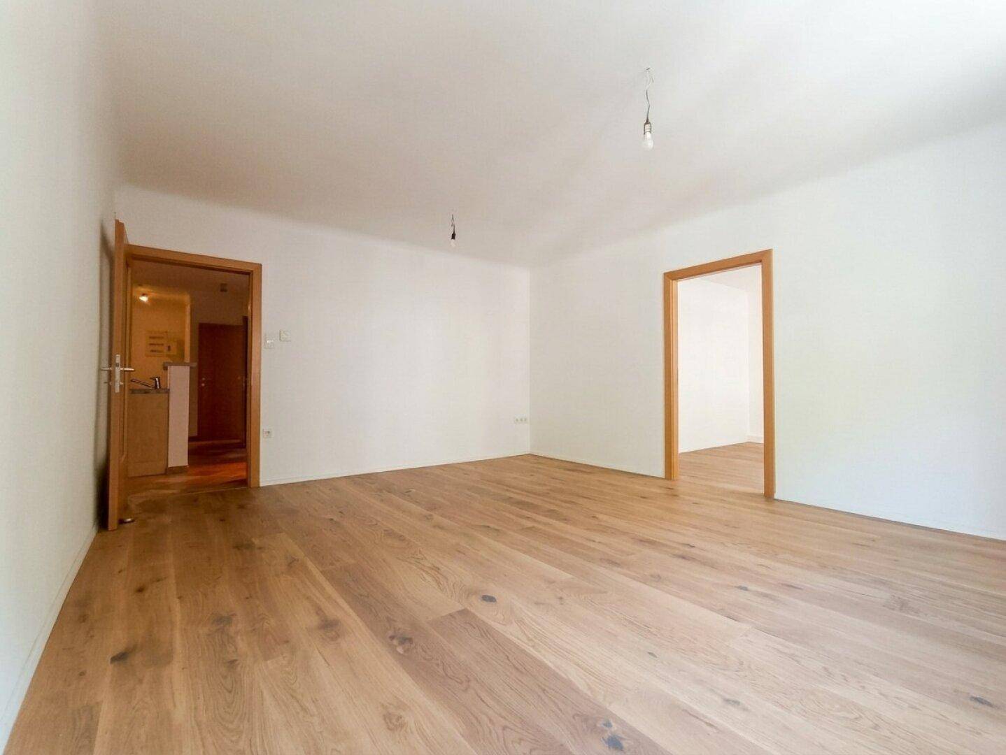 Geräumiges, leeres Zimmer mit Holzboden und zwei Türen, das vielseitig genutzt werden kann.