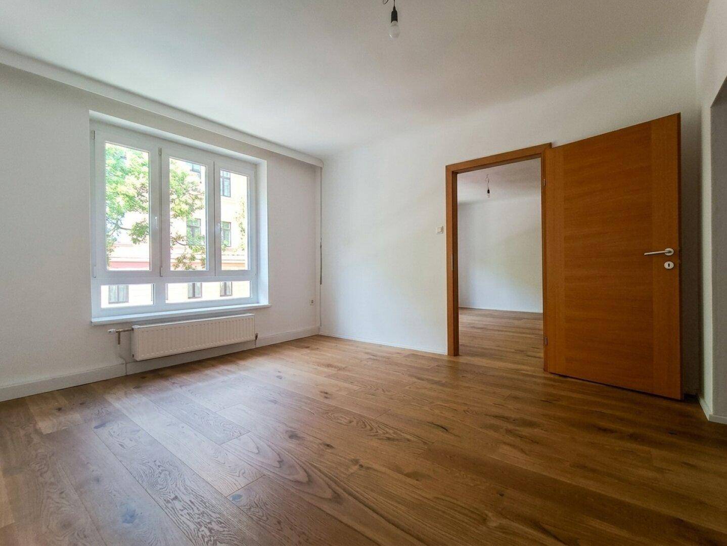Lichtdurchflutetes Zimmer mit neuem Holzboden und Blick ins Grüne durch das große Fenster.